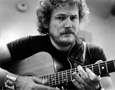 A black and white photo of Gordon Lightfoot  holding a guitar.