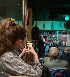 woman uses cell phone to document musical quartet performing on a small stage