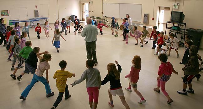 man calling a dance to a circle of children