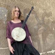 woman wearing a banjo leaning against a wall