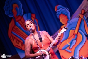 woman playing banjo in front of paintings of women playing music